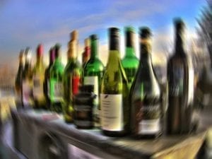 A fuzzy assortment of different bottles of alcohol fills a shelf, outside.